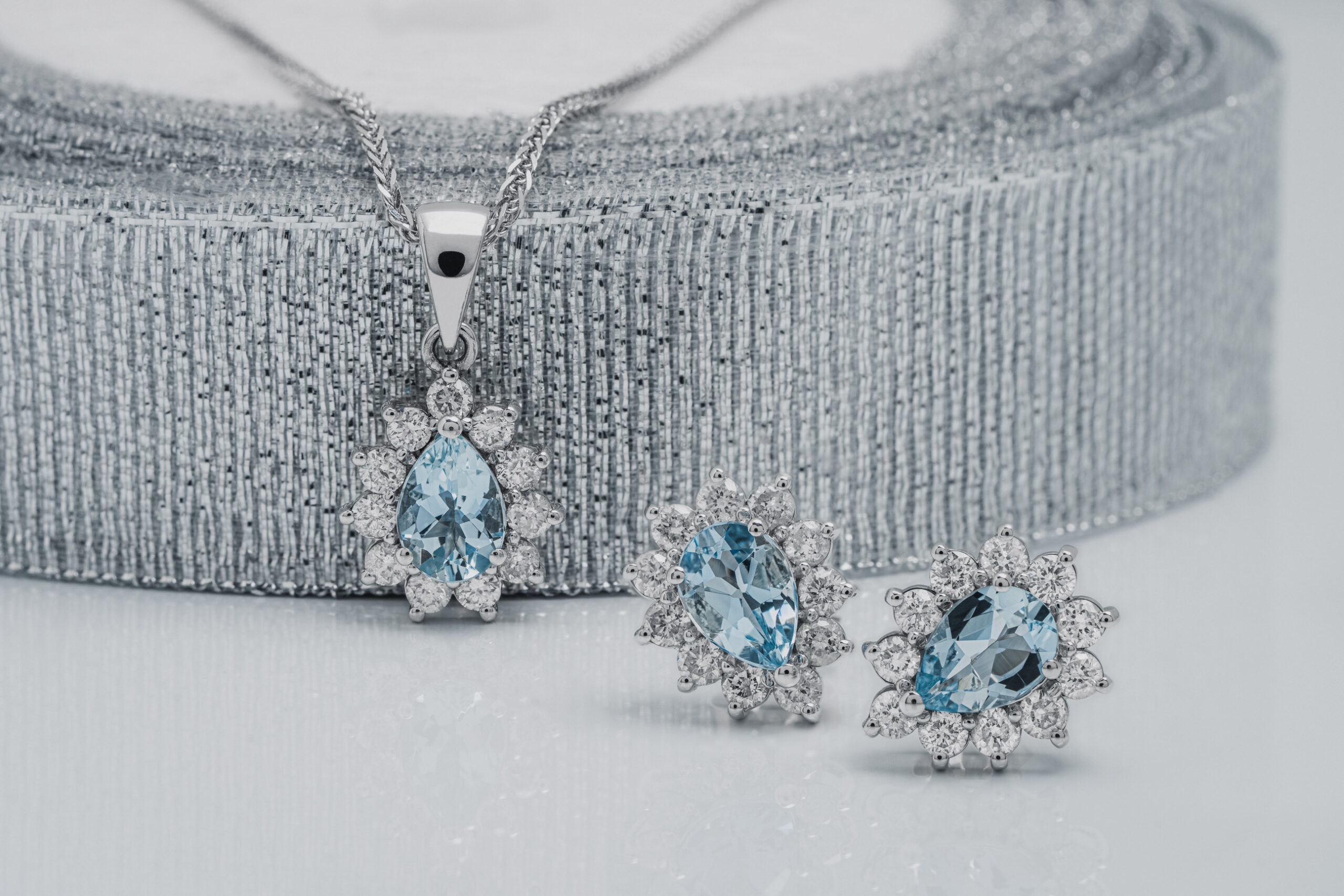 two diamond halo aquamarine earrings beside a diamond halo aquamarine pendant