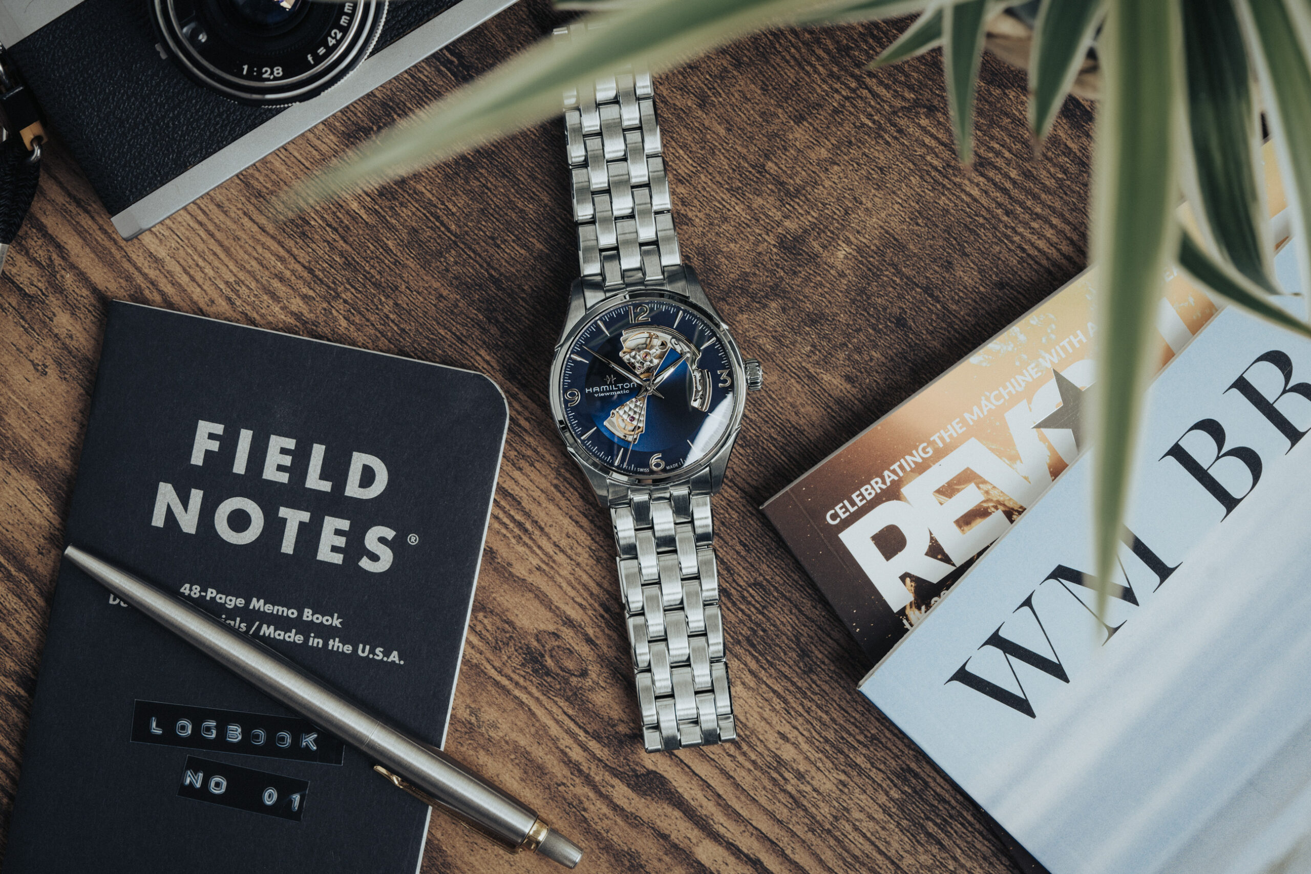Hamilton Jazzmaster open-heart automatic with blue dial on table with revolution magazine and wm brown magazine, beside is a field notes book and pen and film camera
