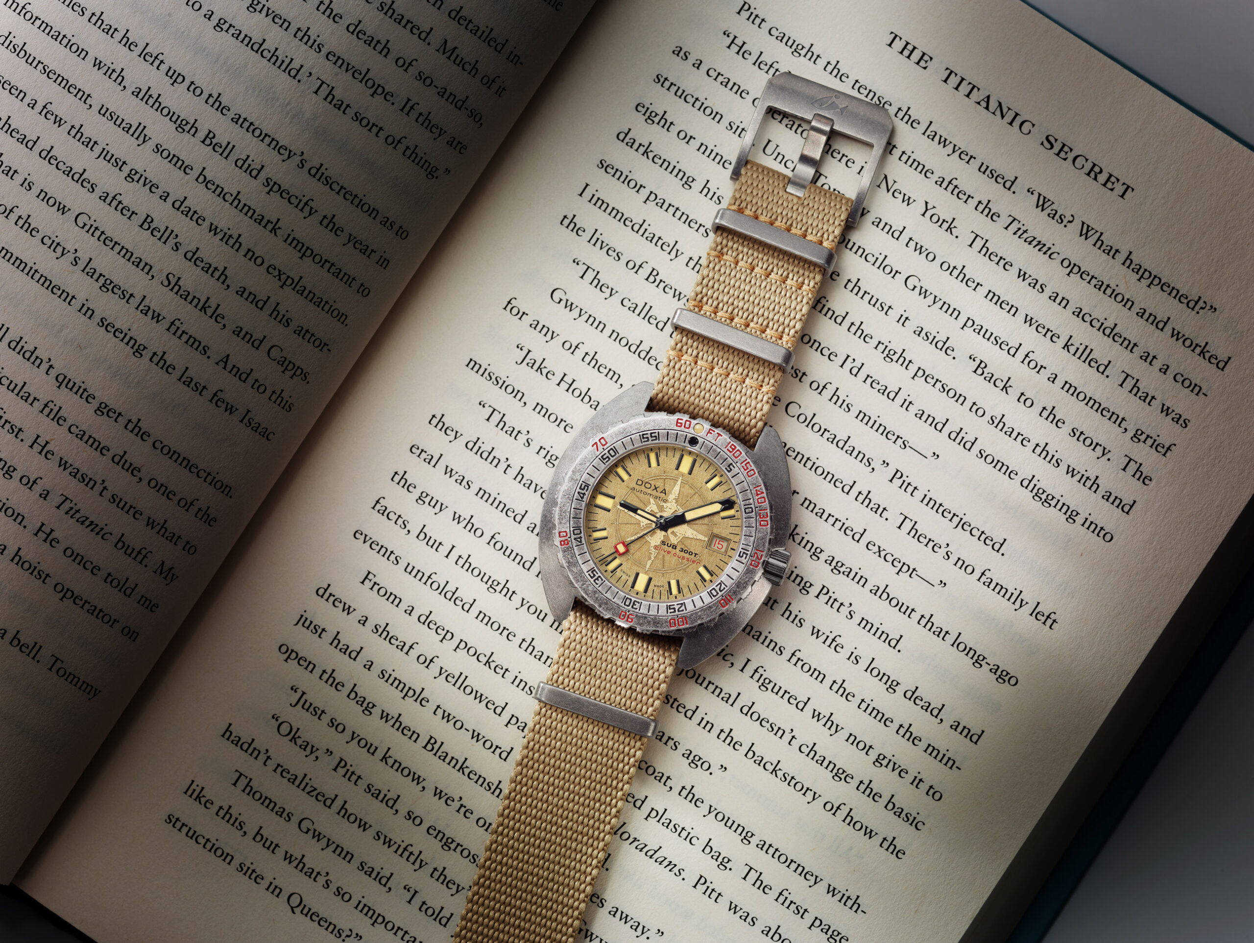 Sub 300T Clive Cussler on beige nato strap lying on book